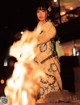 A woman in a kimono standing in front of a fire.