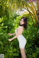 A woman in a white dress posing in front of a palm tree.