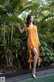 A woman in an orange dress standing next to a pool.