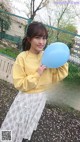 A woman in a yellow sweater holding a blue balloon.