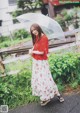 A woman in a red top and white skirt holding an umbrella.