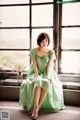 A woman in a green dress sitting on a window sill.