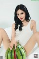 A woman sitting on top of a table next to a watermelon.