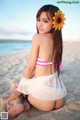 A woman in a bikini sitting on the beach with a flower in her hair.