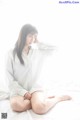 A woman sitting on a bed in a white shirt.