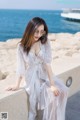 A woman in a white dress sitting on a ledge by the water.