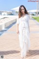 A woman in a white dress standing on a sidewalk.