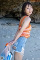 A young woman standing on a beach holding a bag.