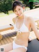 A woman in a white bikini sitting on a yoga mat.